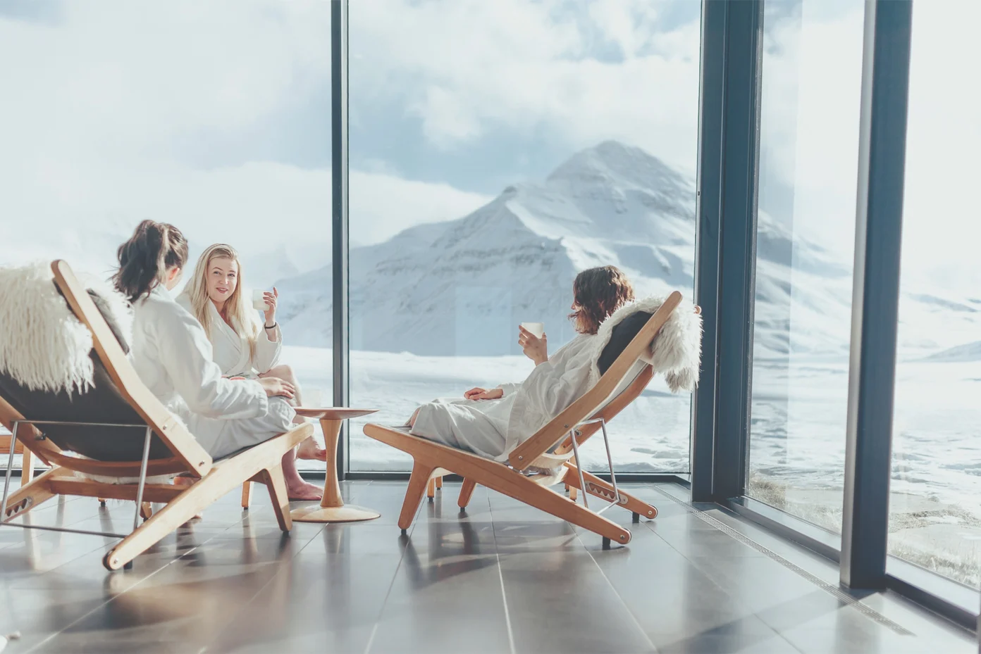 3 people enjoying drinks in spa chairs with views of a mountain.
