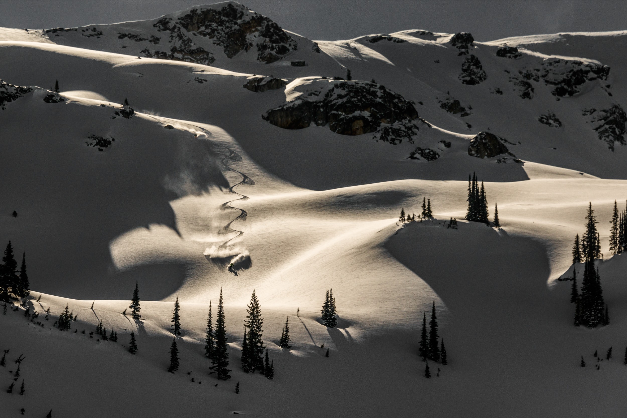 An aerial view of a skier carving S's in the late-day mountain snow.