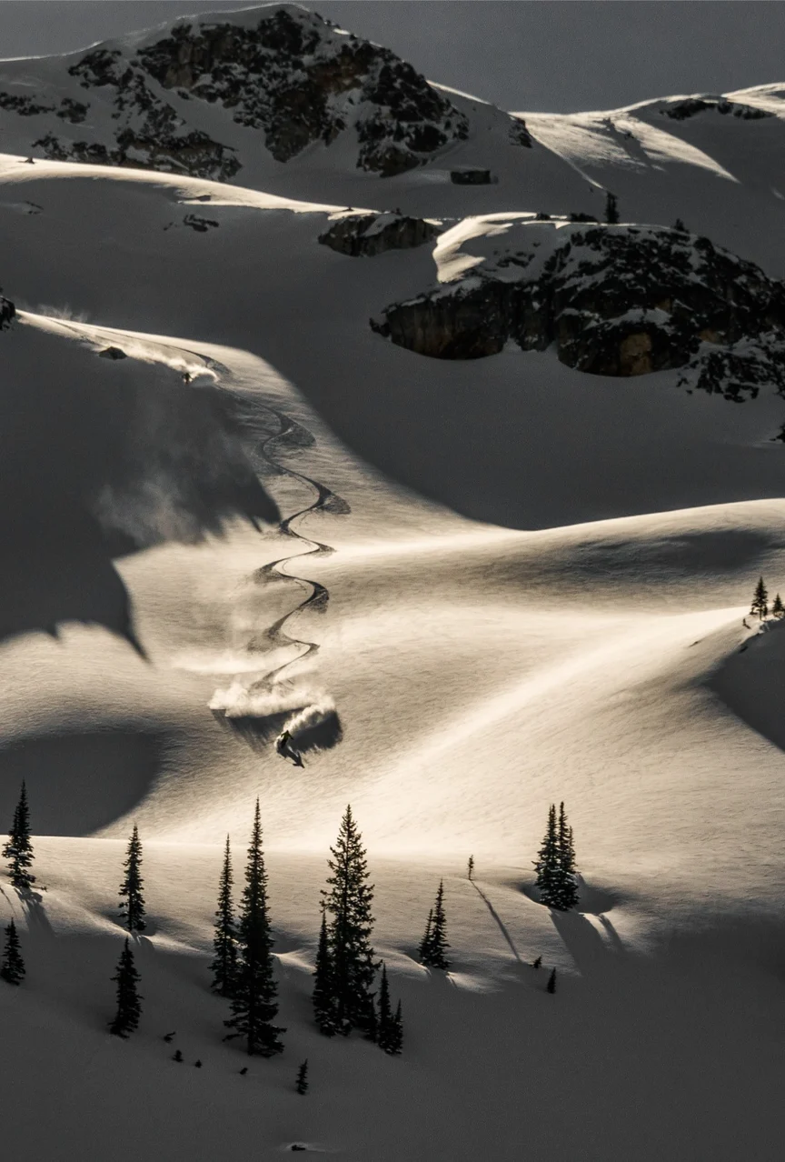 An aerial view of a skier carving S's in the late-day mountain snow.