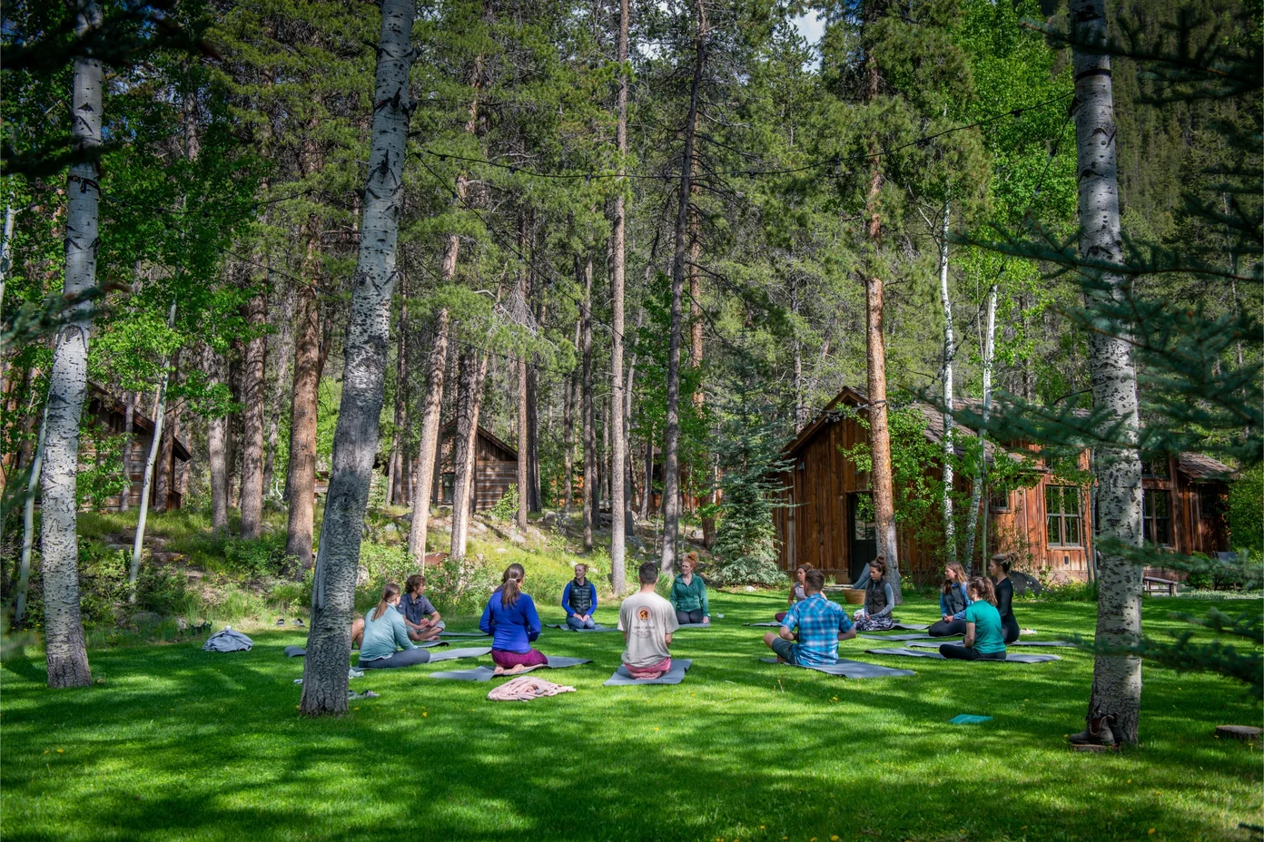 A group meditation on the green grass in the wooded area surrounding Taylor River Lodge.
