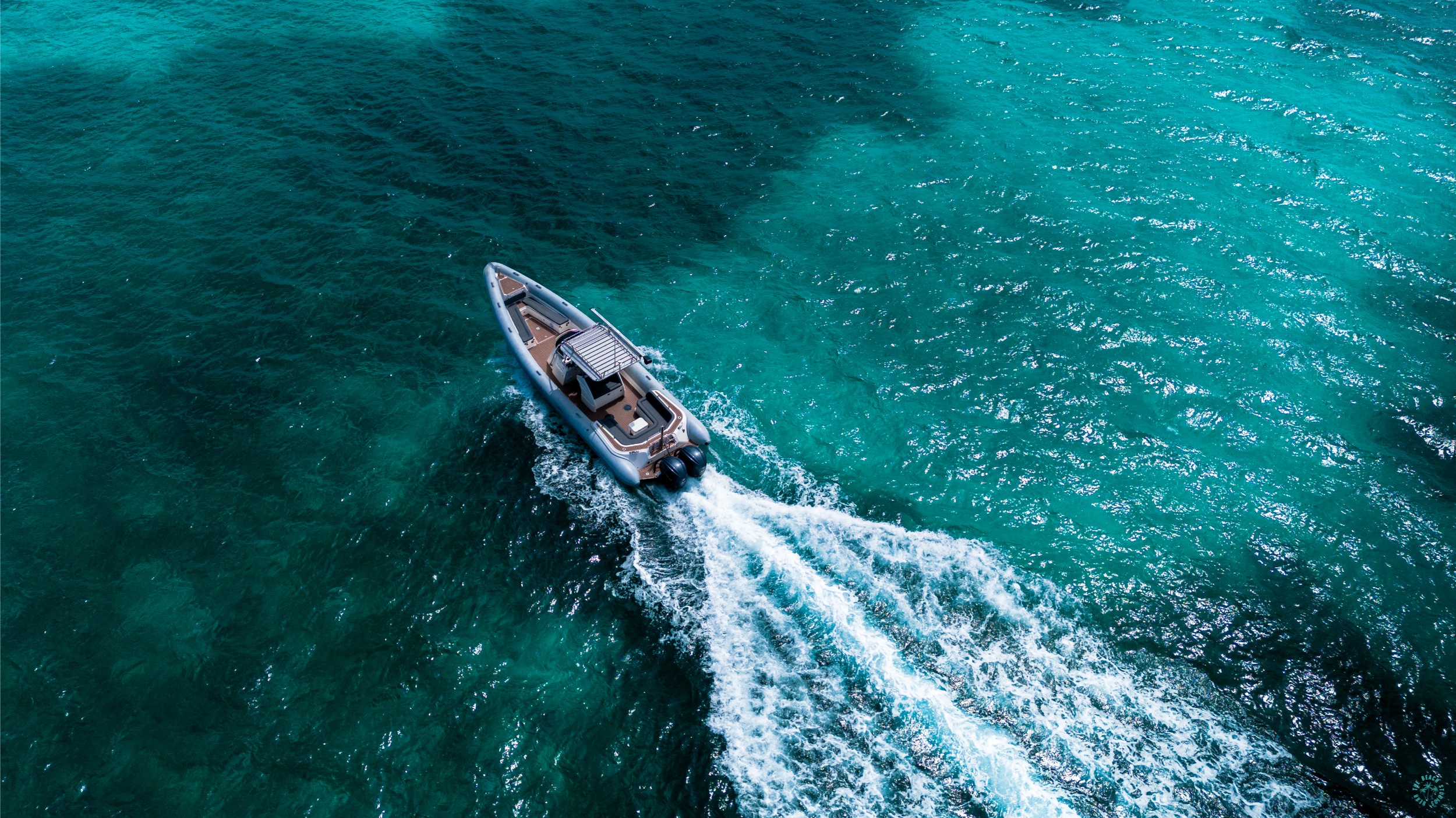 A scorpion rib boat has a wake as it sails through turqouise waters.