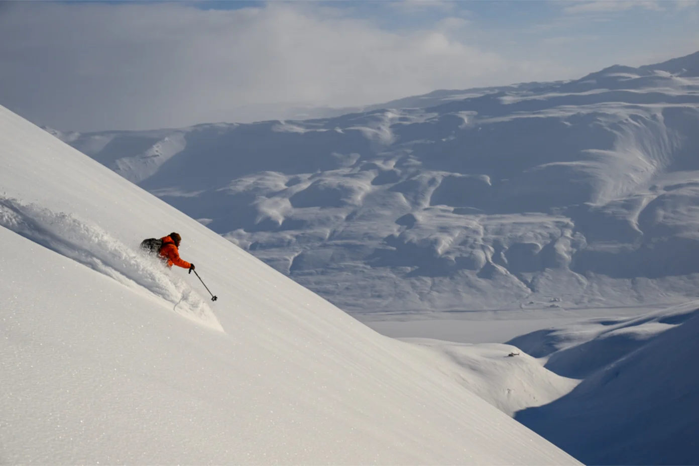 A skier in a snow cloud going downhill in an Icelandic mountain range.
