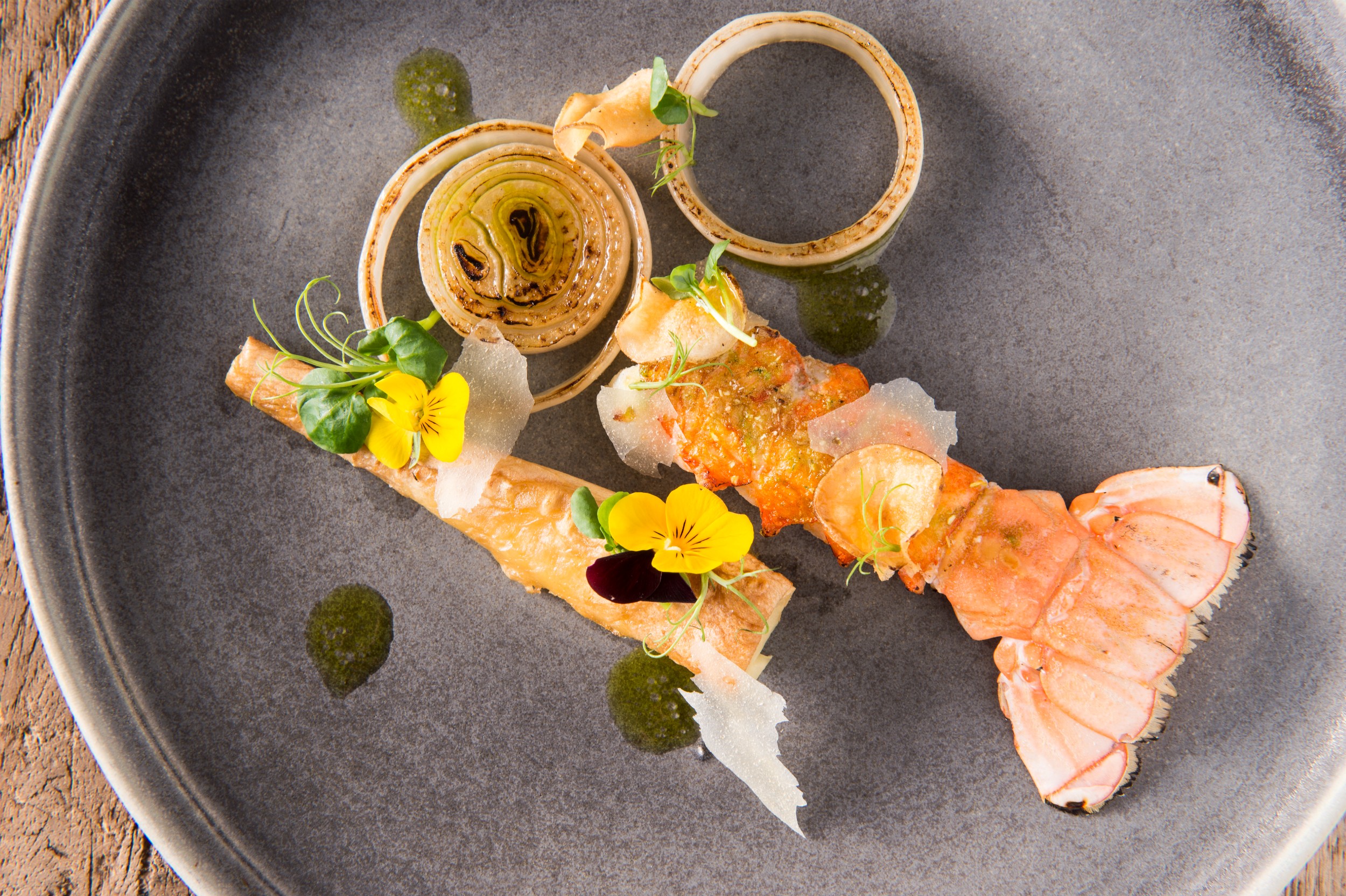 A plated lobster tail with various flowers and adornments.
