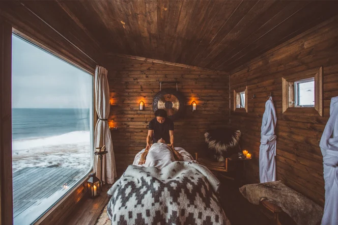 A person receiving a message wrapped in blankets in a cozy wood-sided room with a view of water outside.