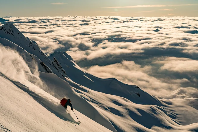 A person skiing at dusk above the clouds.
