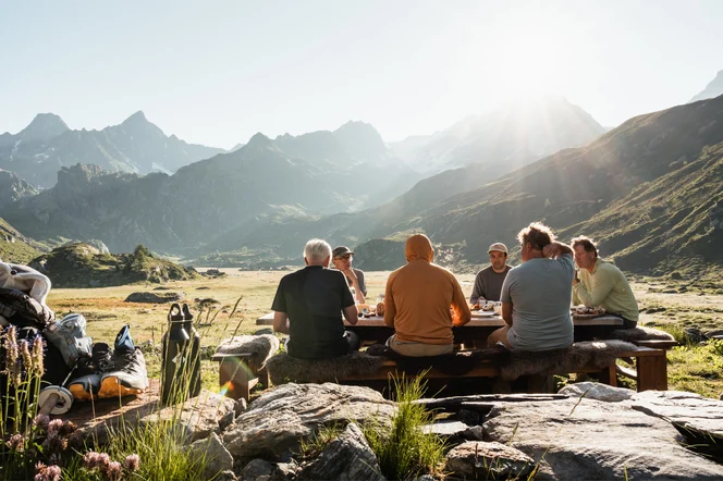 A group of hikers enjoying lunch at an outdoor table in a valley.