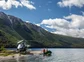 A helicopter parked in a remote river valley with two fishers on a small boat.