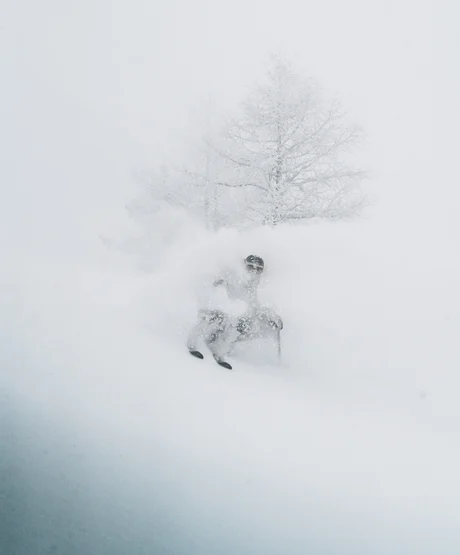 A skier in a cloud of snow headed down a near vertical slope.