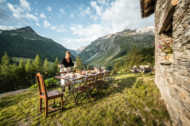 A person preparing an outdoor meal at a hiking hut in the Alps.