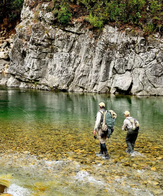 Two people wearing waders fly fishing in the middle of Owen River.