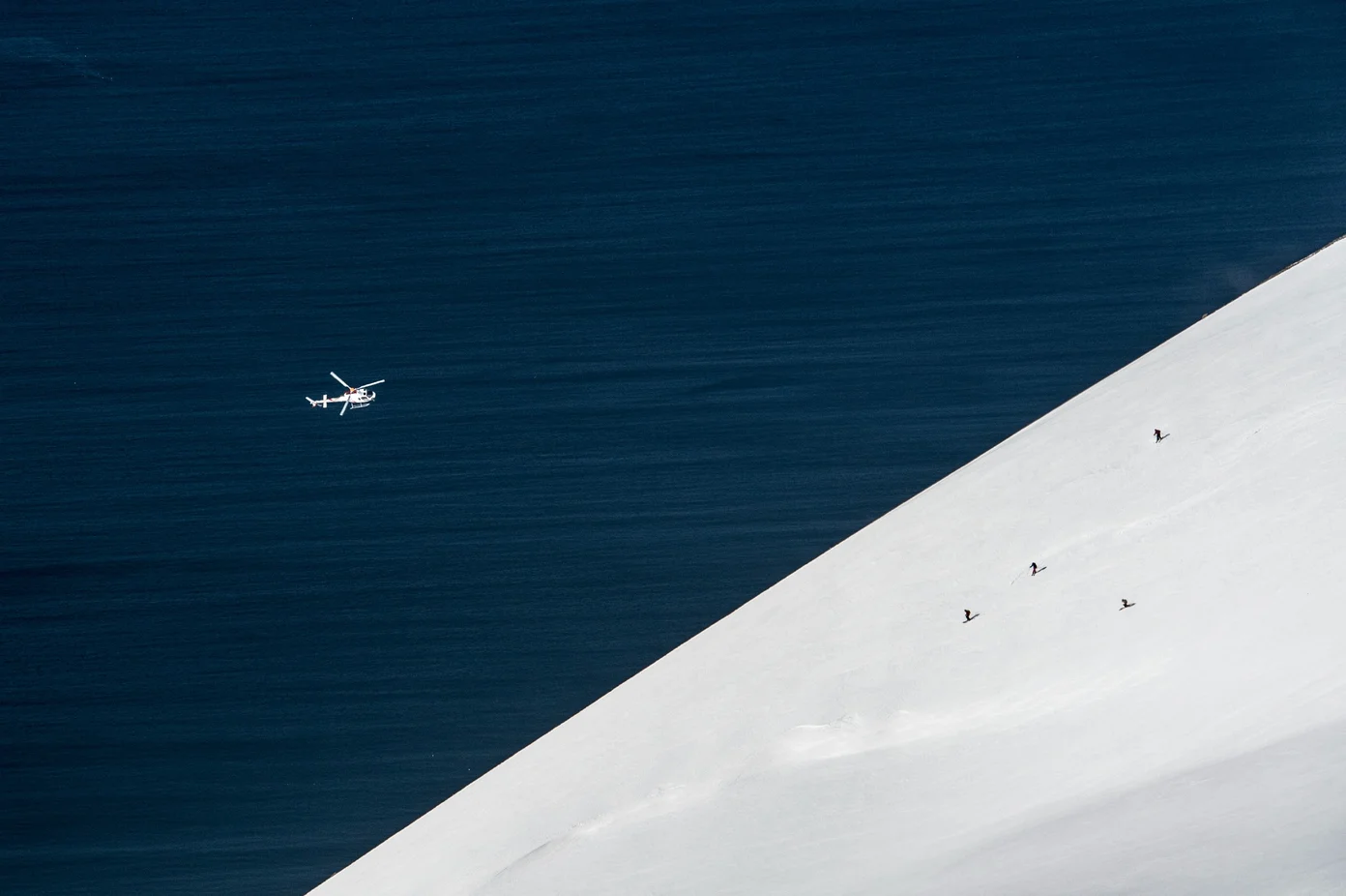 An aerial view of a helicopter flying over head and three skiers.