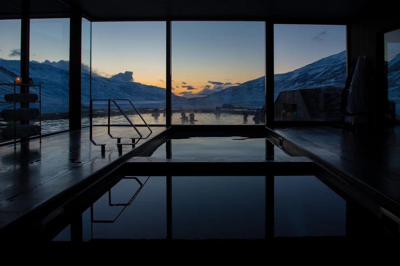 A view of the indoor hot tub and a group of people in the outdoor heated pool at sunset.