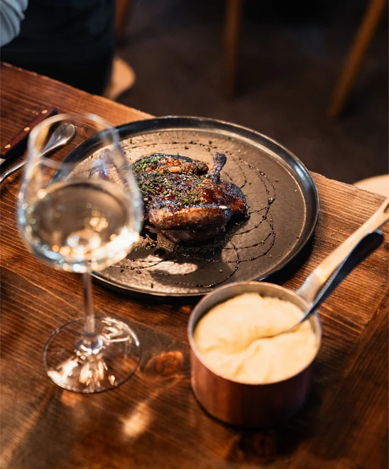 A plated roast chicken with mash potatoes and a glass of wine.