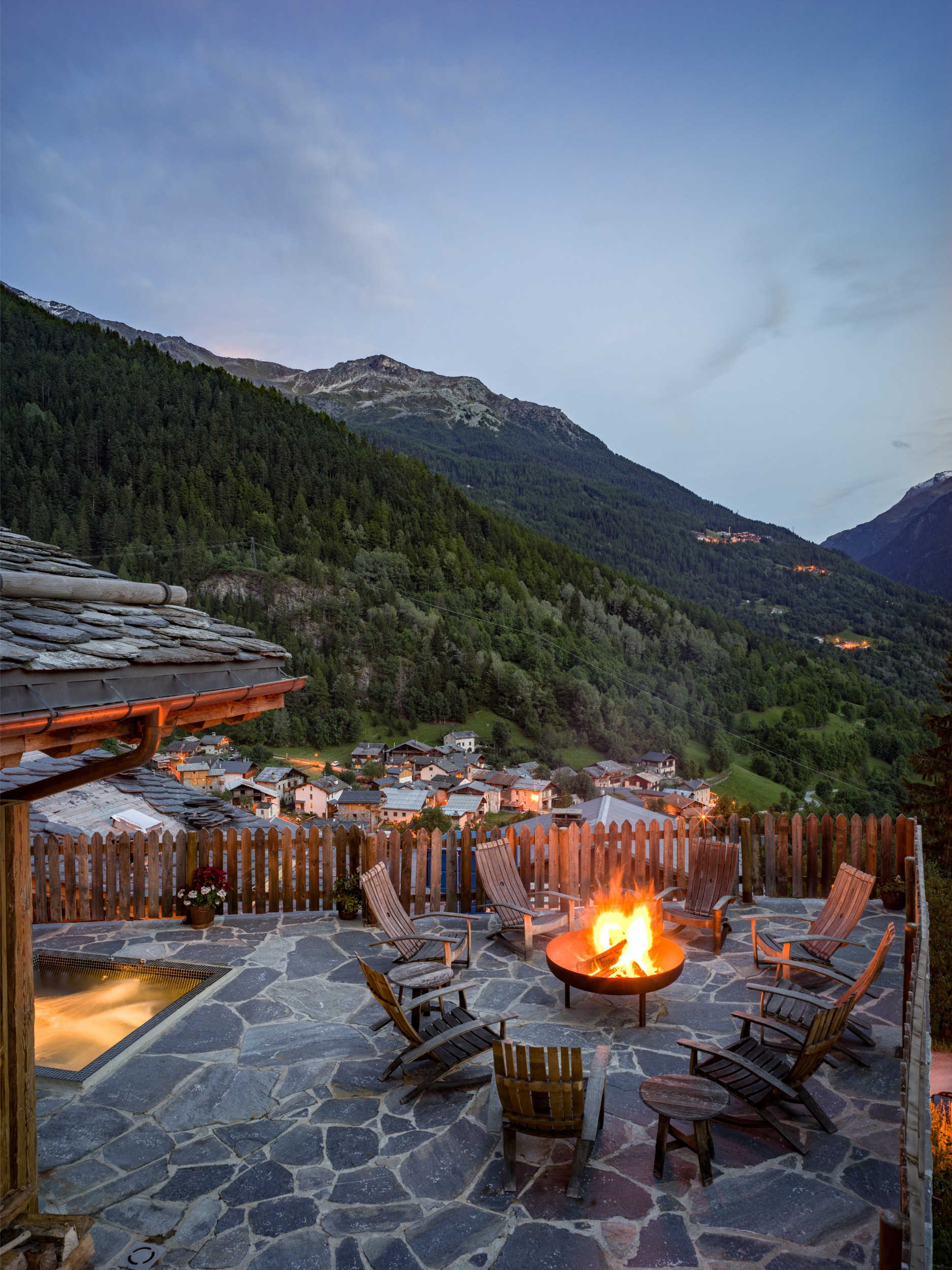 A patio with a fire pit overlooking a mountain valley and small village.