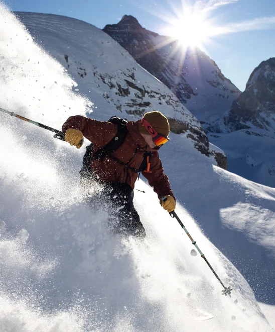 A skier in a cloud of snow headed down a near vertical slope.