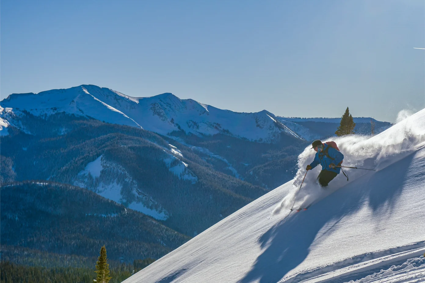 A skier carving near the top of a mountain with a view of a mountain range.