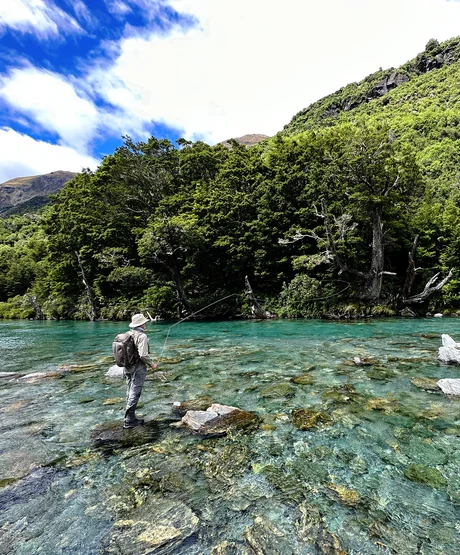 man fishing on rocks by mountainside