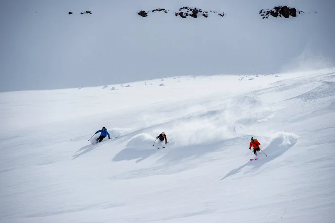 Three skiers headed down a powdery mountain in Iceland.