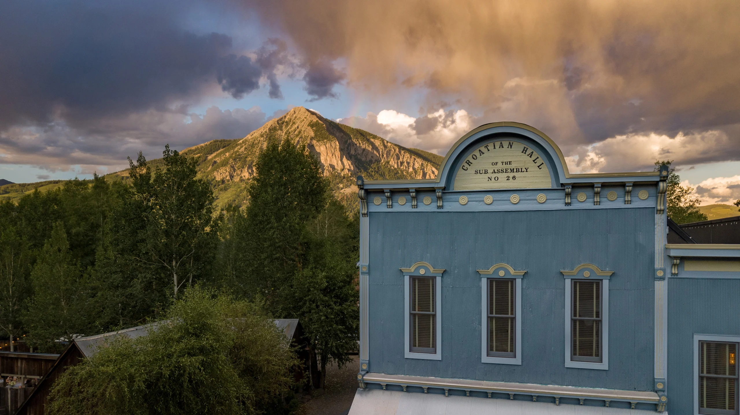 The top portion of the Old Croation Saloon, now Scarp Ridge Lodge on a summer day, with a mountain and rainbow in the background.
