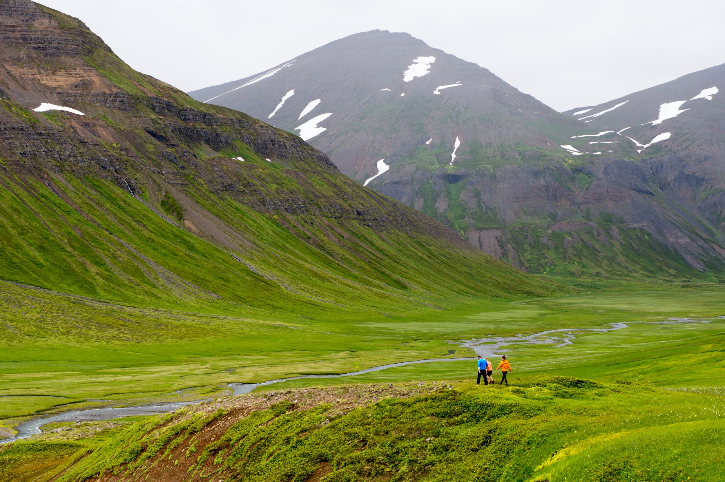 Two hikers in Iceland walking in a valley with a creek and steep mountains.