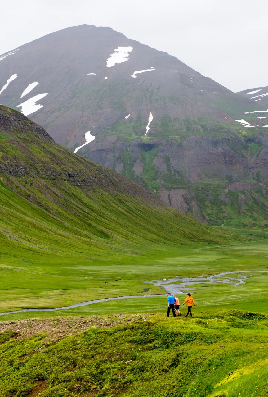 Two hikers in Iceland walking in a valley with a creek and steep mountains.
