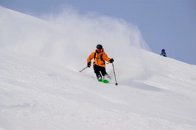 A skier in a bright orange coat headed down a mountain.