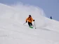 A skier in a bright orange coat headed down a mountain.