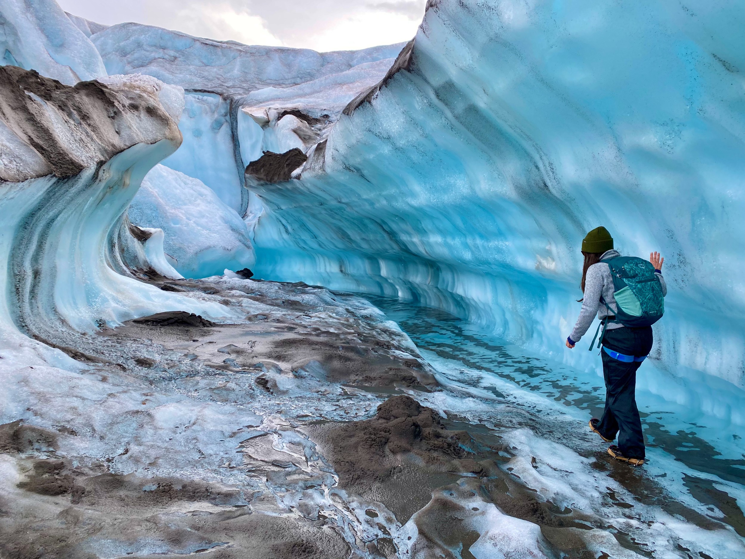 A person walking along a large formation of a glacier.