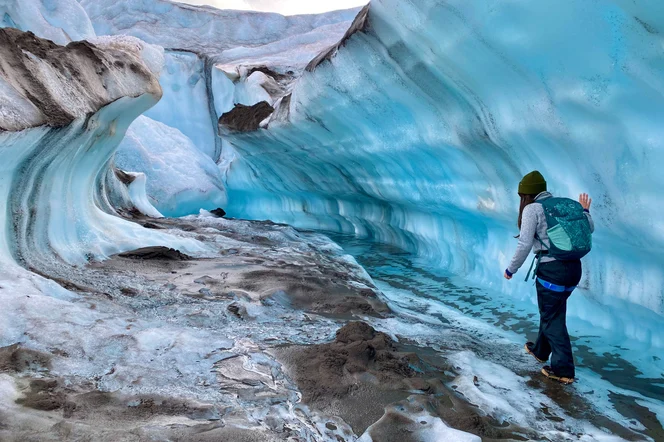 A person walking along a large formation of a glacier.