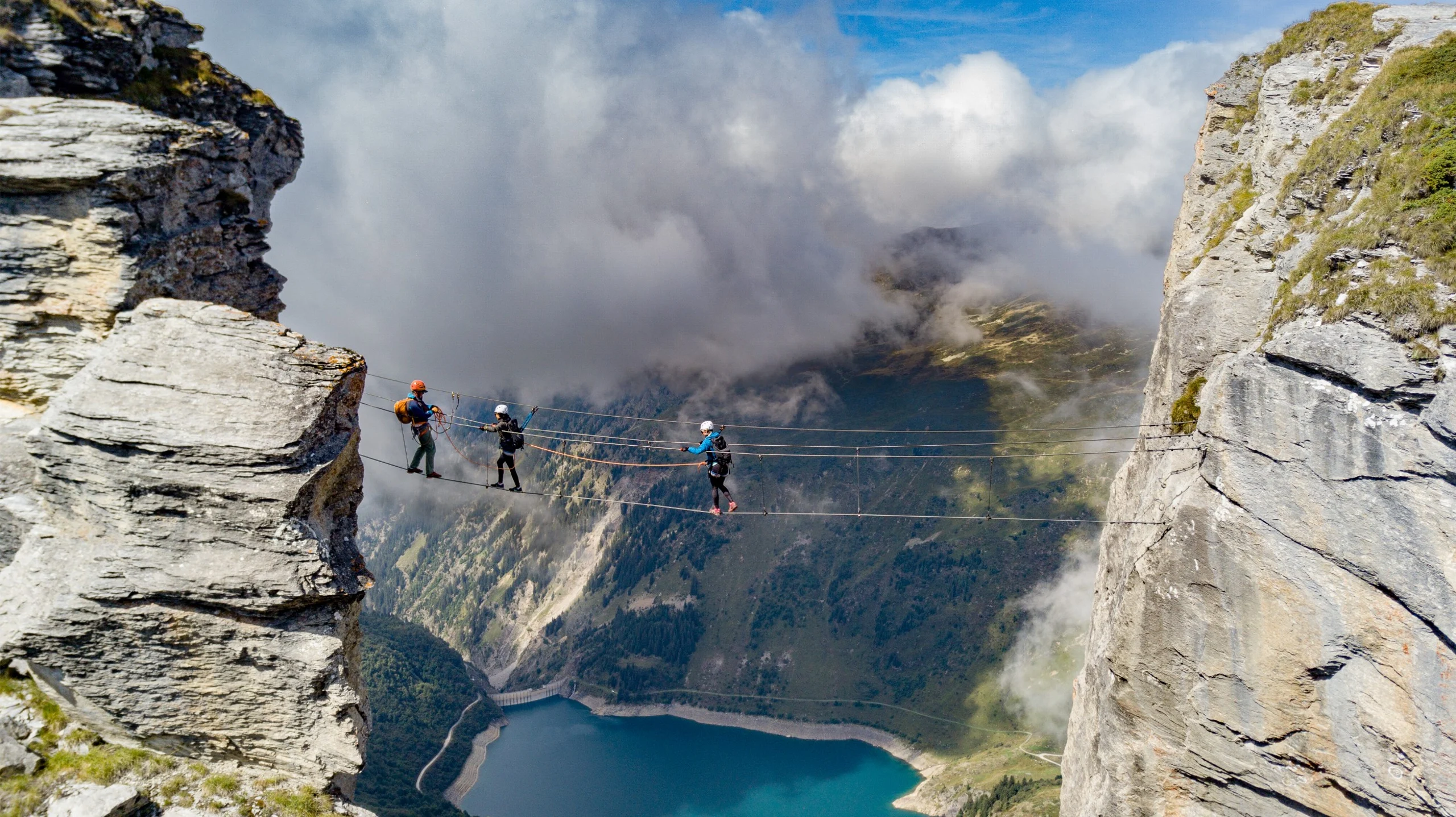 A group of climbers crossing a large gap between cliffs on a rope bridge.