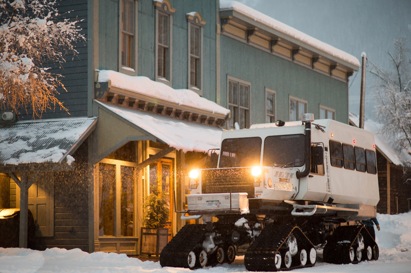 A snowcat with it's light on sits outside of the historical Eleven Scarp Ridge Lodge.