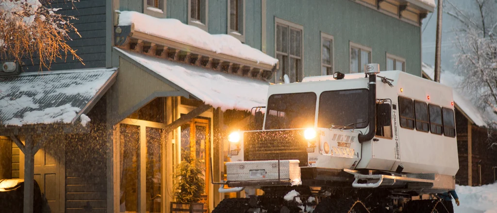 A snowcat with it's light on sits outside of the historical Eleven Scarp Ridge Lodge.