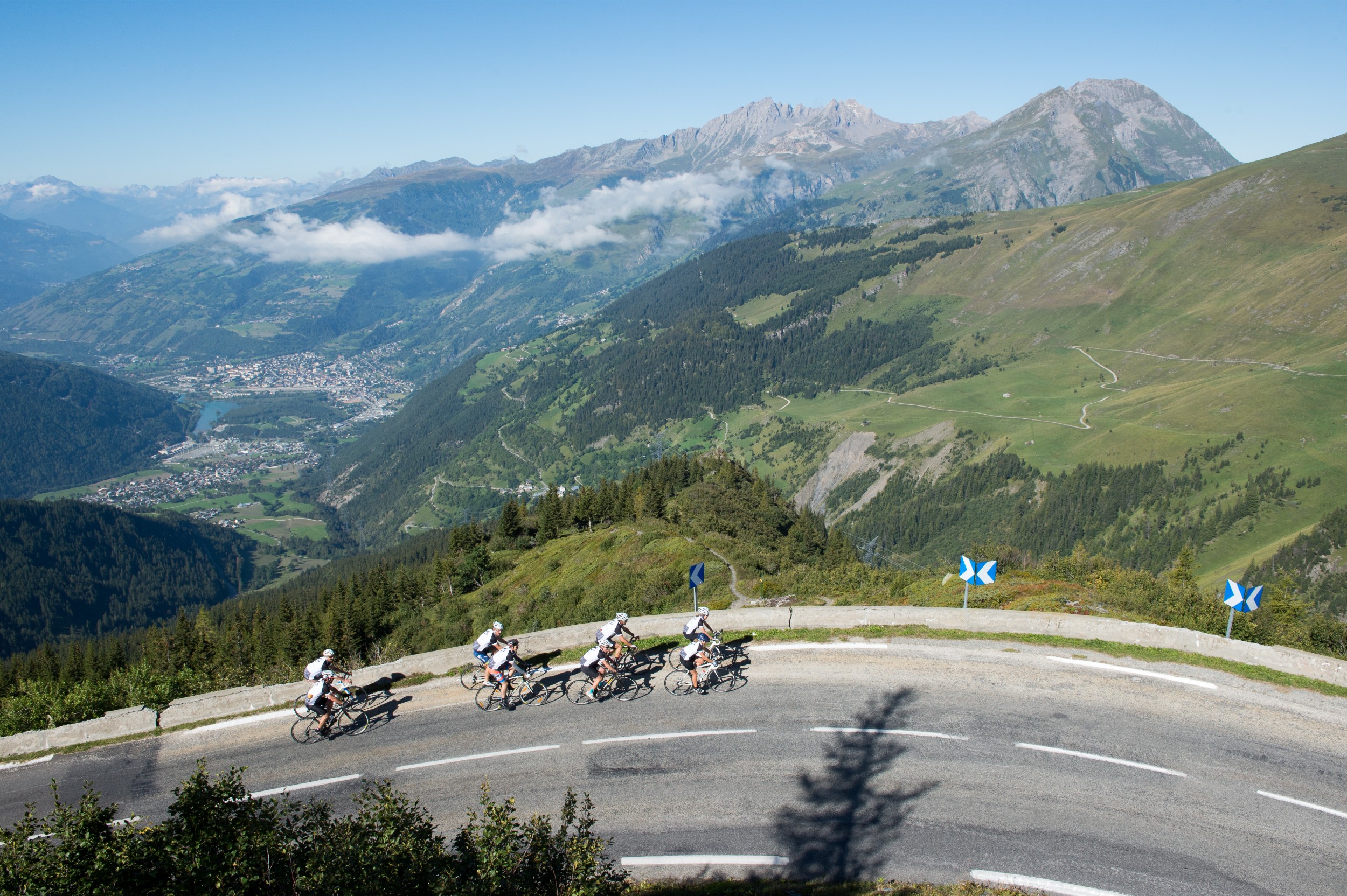 A large group of cyclists headed around a bend on road in the Alps.