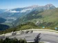 A large group of cyclists headed around a bend on road in the Alps.