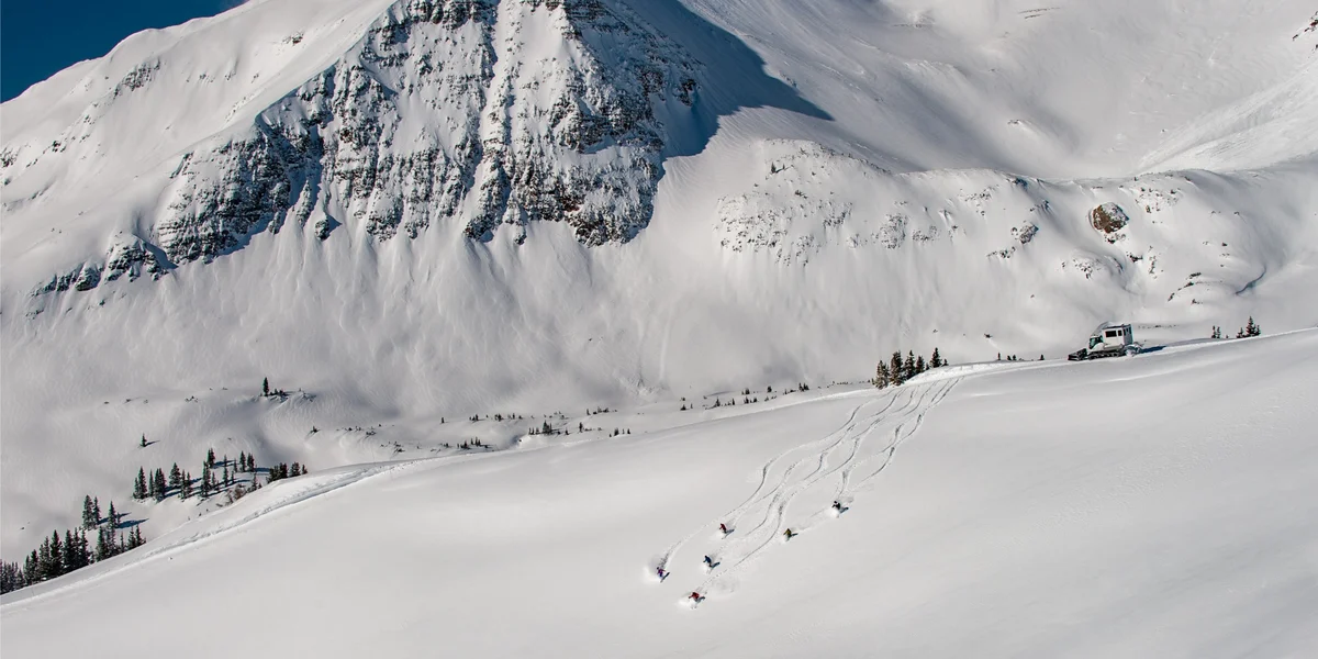 Group of people skiing atop a tall snow covered mountain.