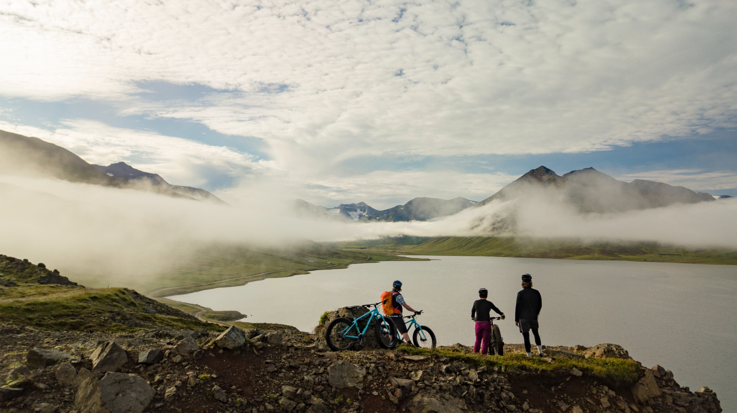Three bikers overlooking a lake surrounded by mountains in Iceland.