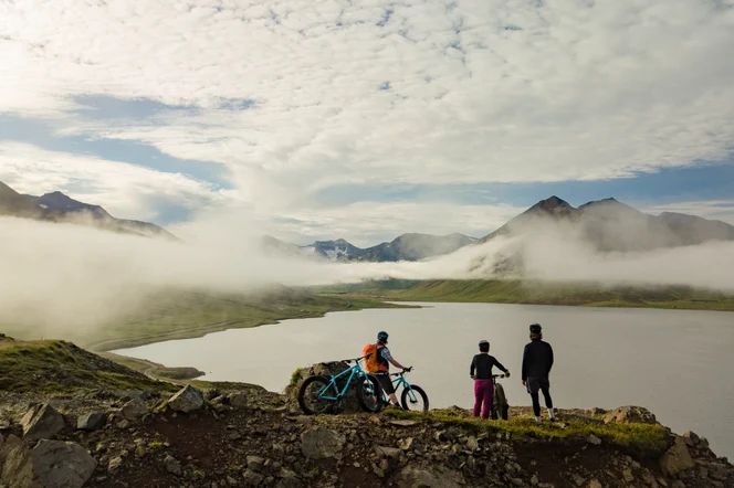 Three bikers overlooking a lake surrounded by mountains in Iceland.
