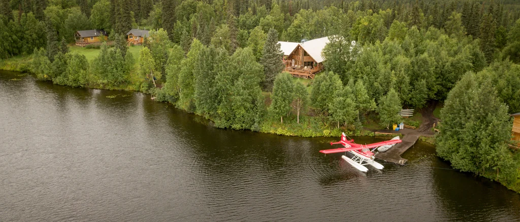 Exterior of a log cabin, Eleven Winterlake Lodge, surrounded by trees with a lake in front.