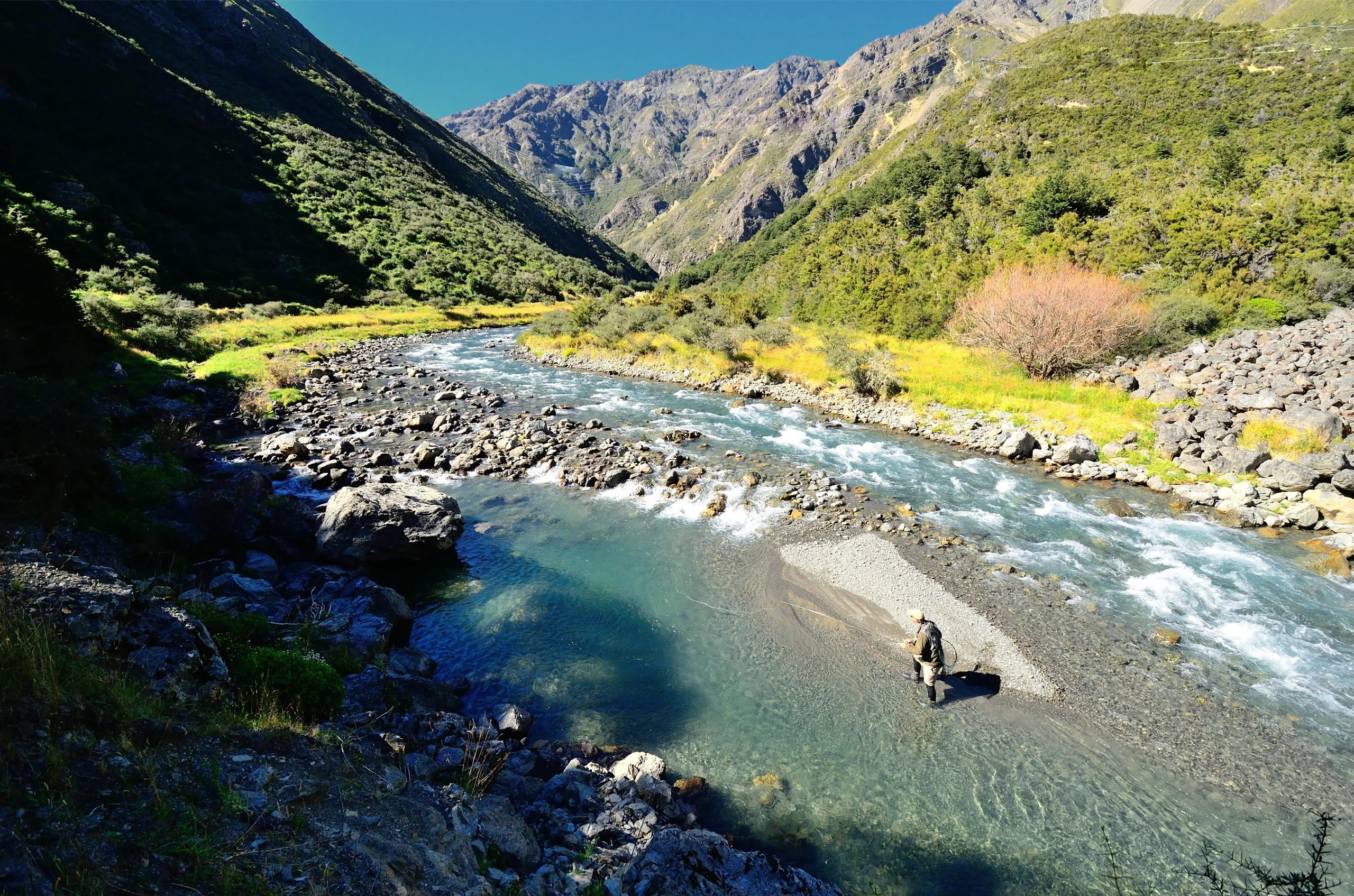 A person standing in the middle of Owen River, fly fishing.