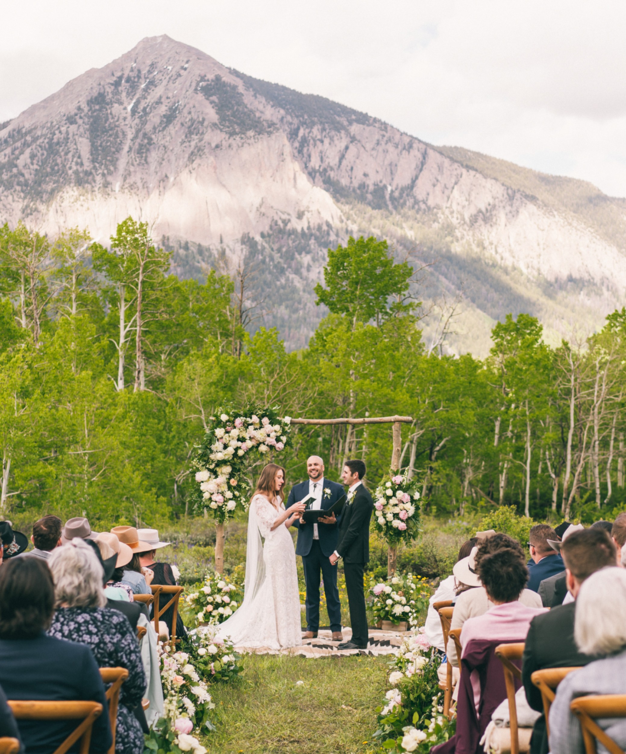 A soon-to-be husband and wife exchanging vows at their wedding ceremony and a mountain in in the distance.
