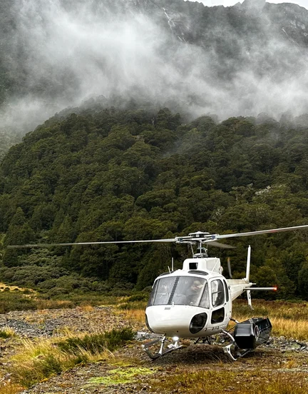 A landed helicopter sitting atop a clouded mountain.