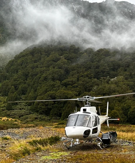 A landed helicopter sitting atop a clouded mountain.