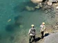 AN overhead shot if two people reeling in a brown trout in clear blue water.