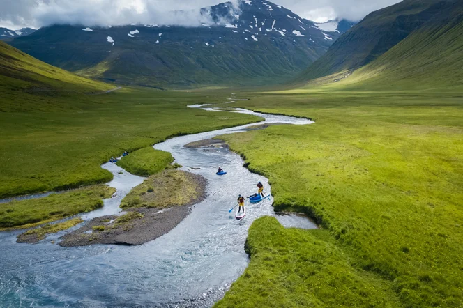 A few people on stand up paddle boards on a creek in Iceland.