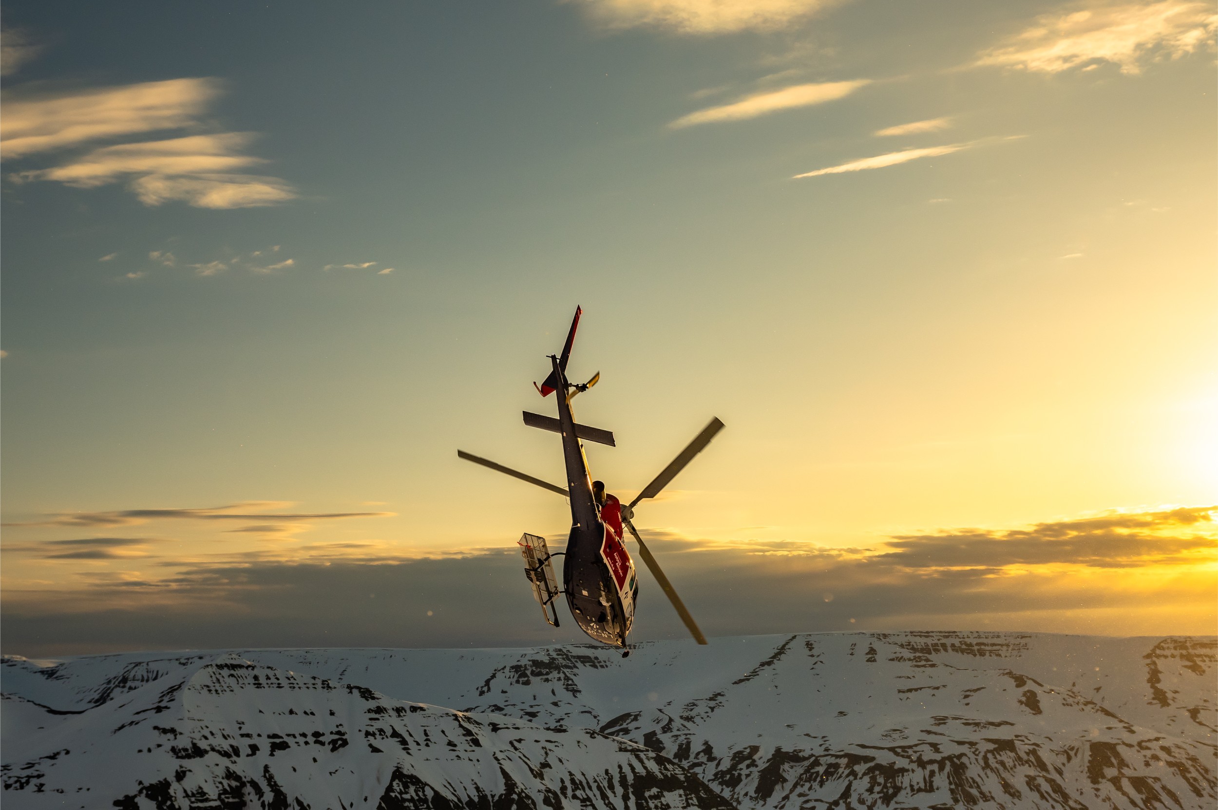 A helicopter over snow mountains performing an aerial maneuver.