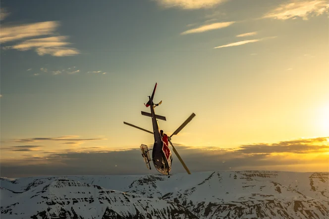 A helicopter over snow mountains performing an aerial maneuver.