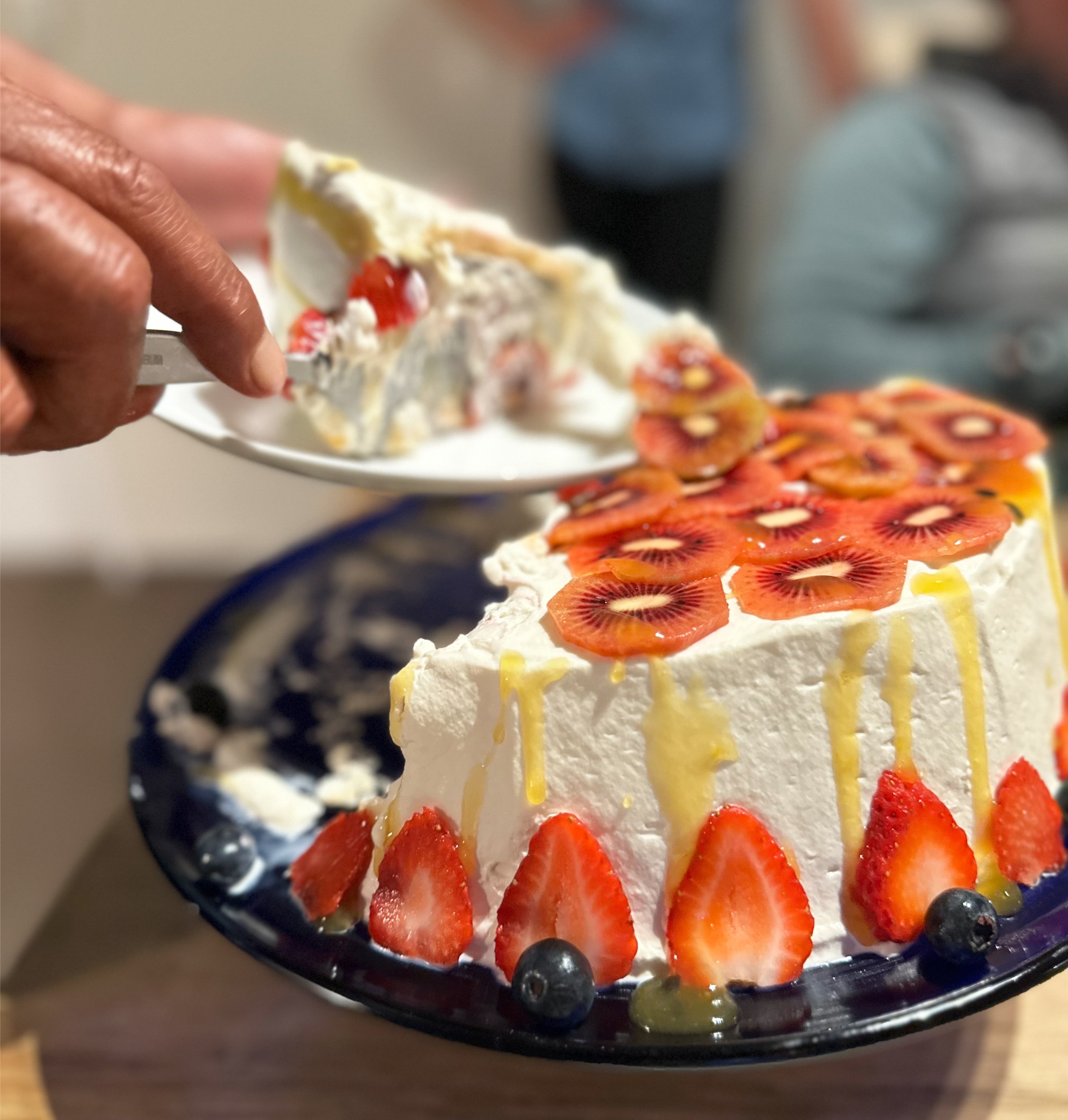 A cake with kiwi, and strawberries being cut and served.