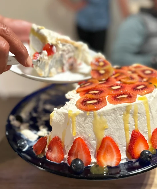A cake with kiwi, and strawberries being cut and served.