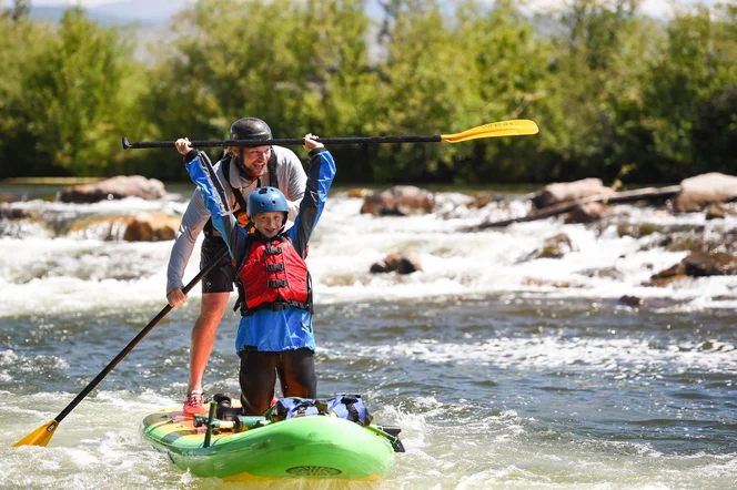 A guide and a child learning how to ride a stand up paddle board.